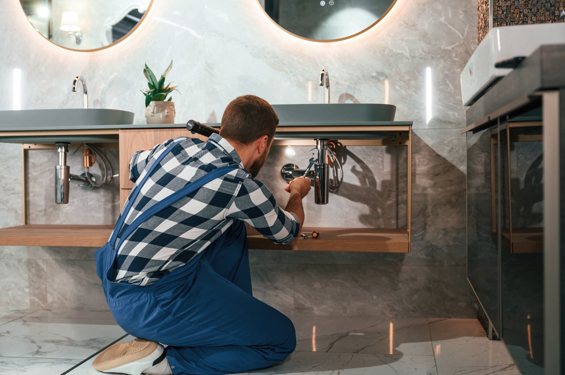 Plombier travaillant sous un évier dans une salle de bain moderne